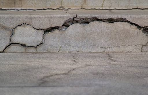 Deep horizontal and stair-step cracks running through a settling concrete foundation wall